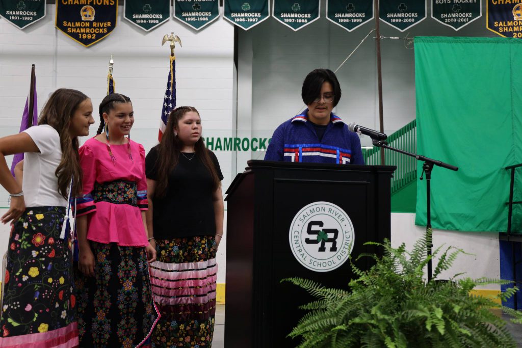 A student speaks at a podium in the ice area while three other students look on