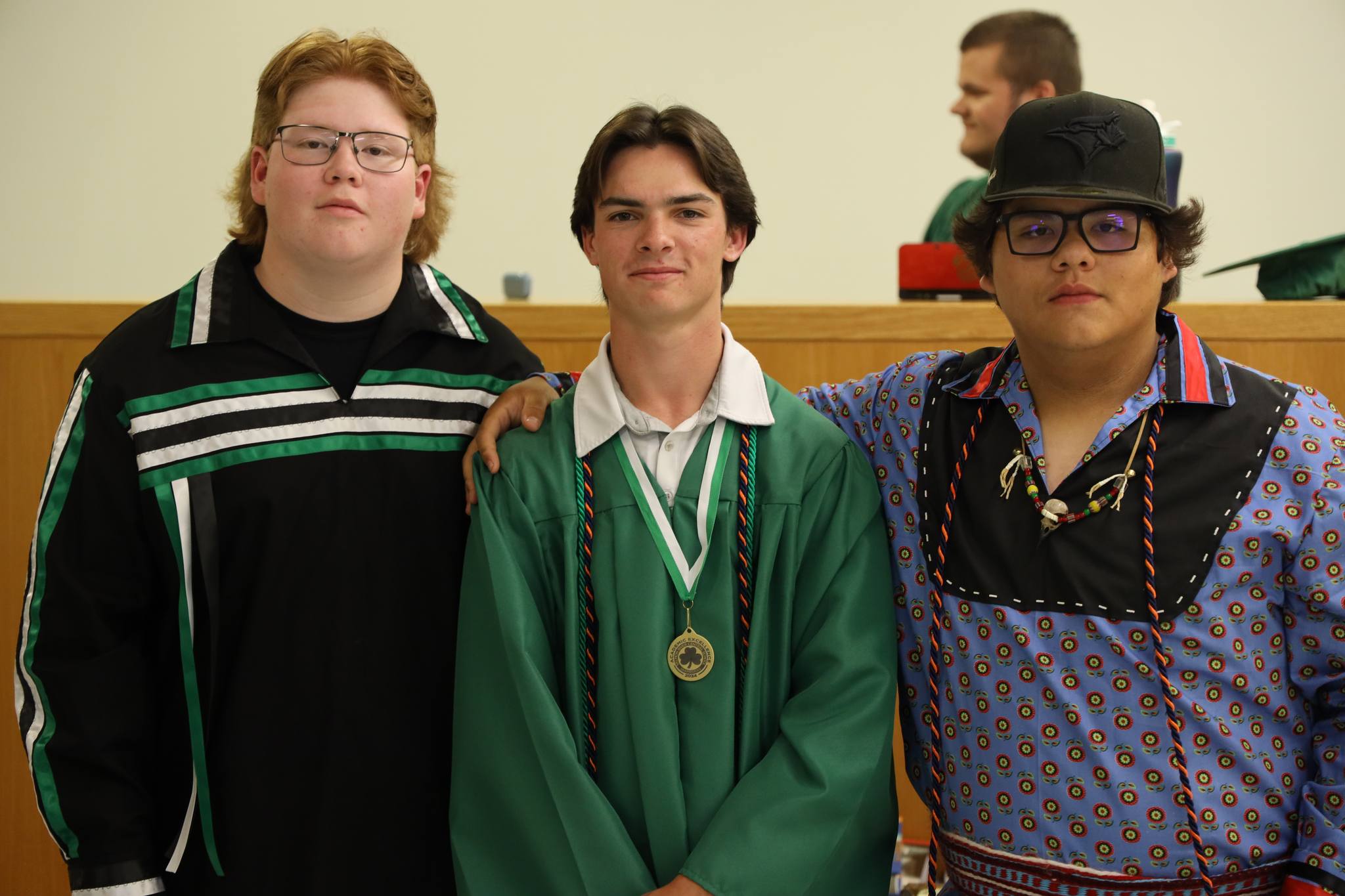 Three students, two in native dress stand together before the graduation ceremony