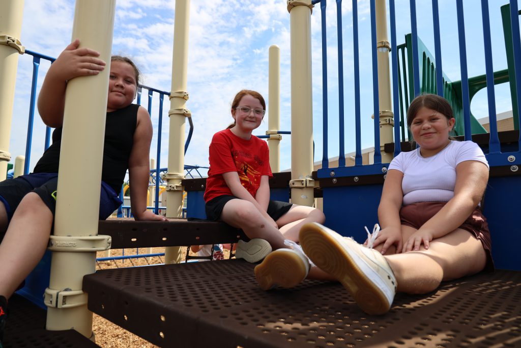 Three girls sitting on a playground posing for a photo