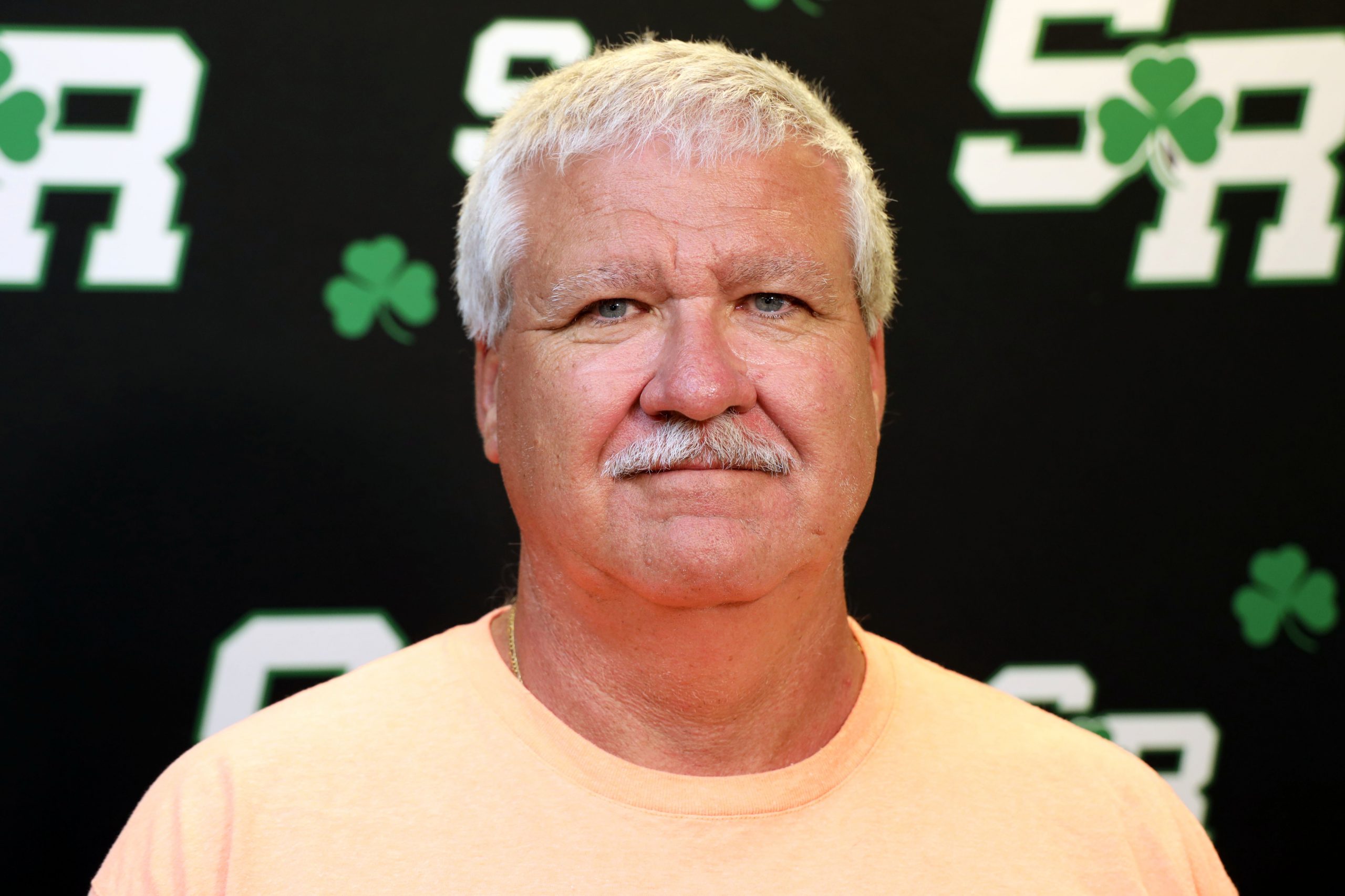 Man smiling in front of a back drop with the letters SR on it