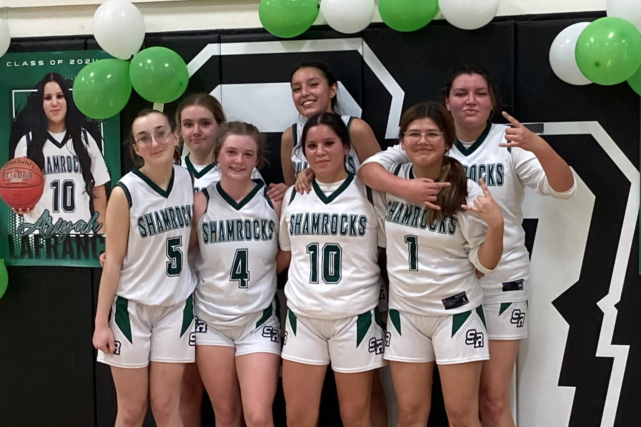 Seven high school athletes pose together with green and white a balloons