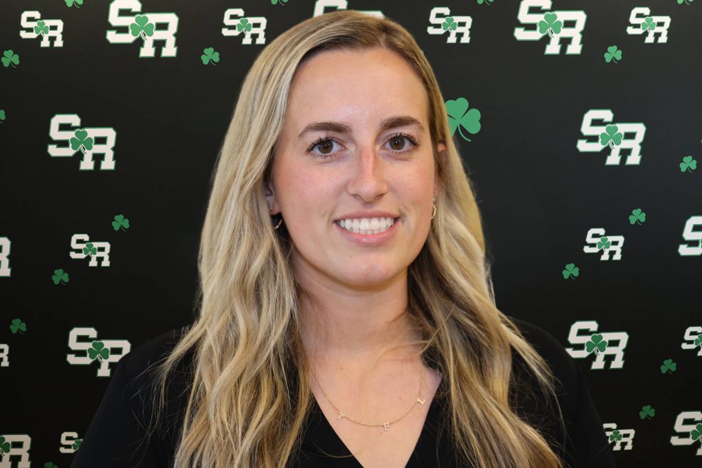 A woman smiling for a photo with a black background with green highlights with the letters 'SR'