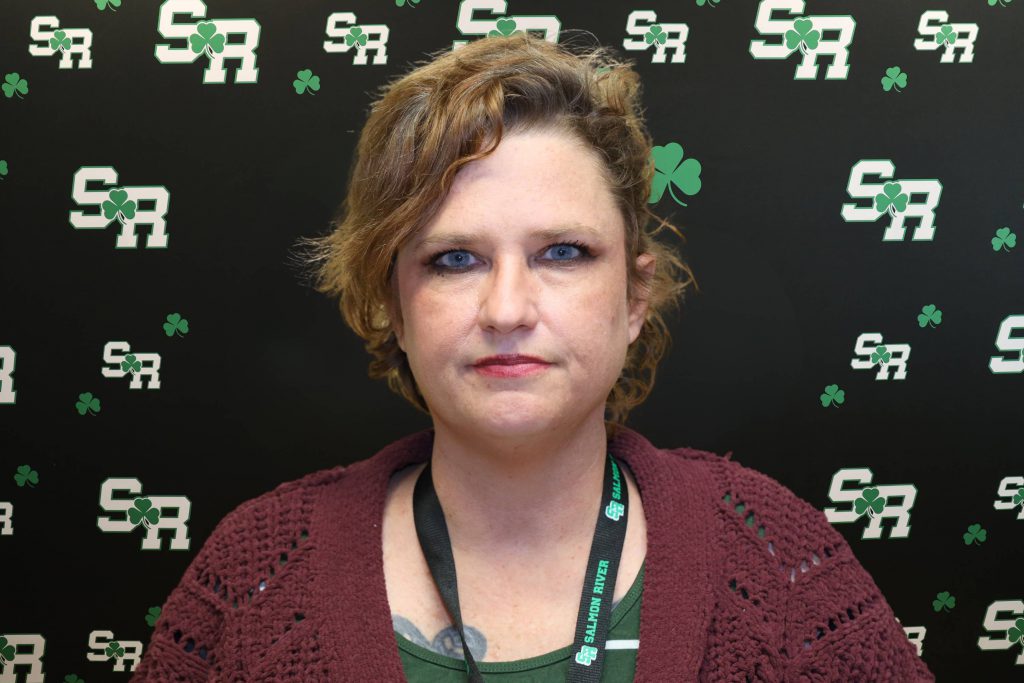 A woman smiling for a photo with a black background with green highlights with the letters 'SR'