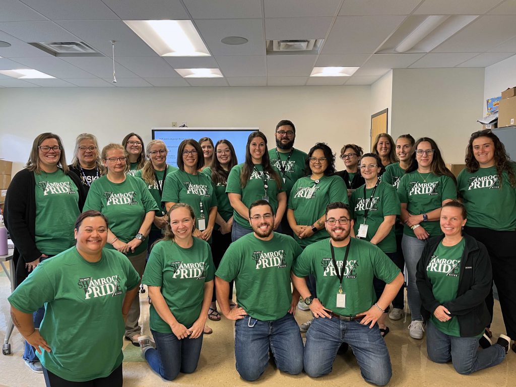 22 people posing for a photo with some people standing and others kneeling wearing the same green t-shirt that says 'Salmon River Shamrock PRIDE'