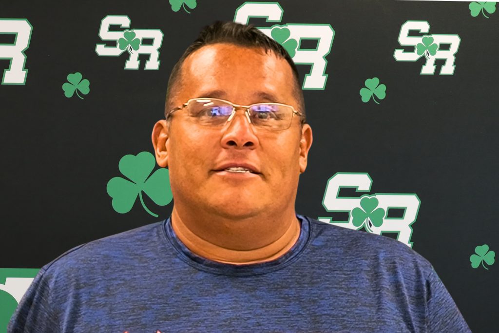 Man smiling in front of a back drop with the letters SR on it