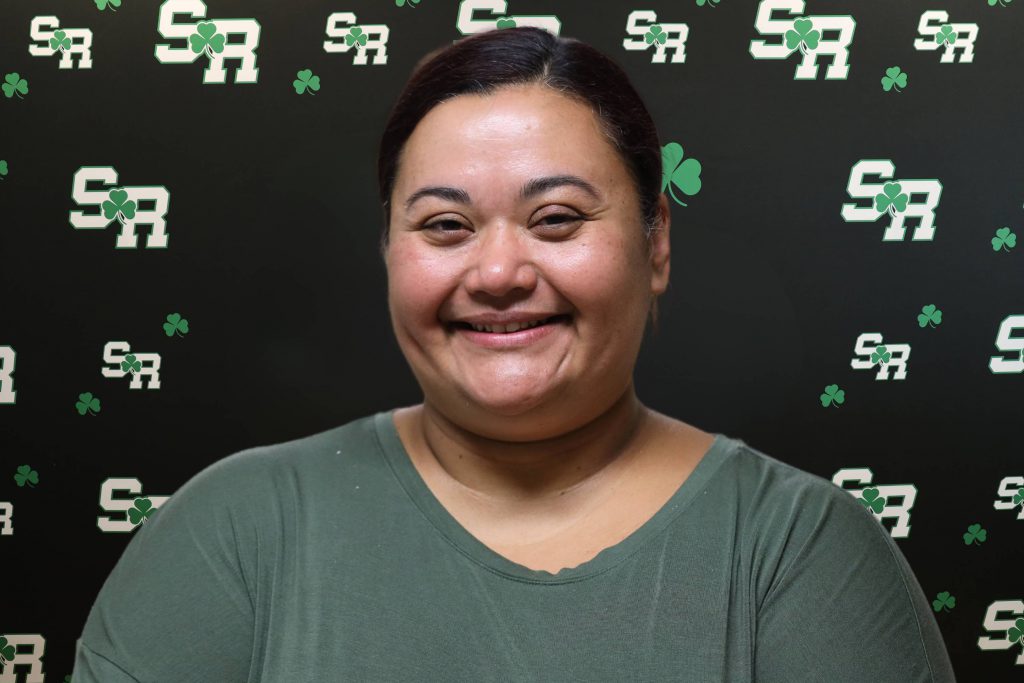 A woman smiling for a photo with a black background with green highlights with the letters 'SR'