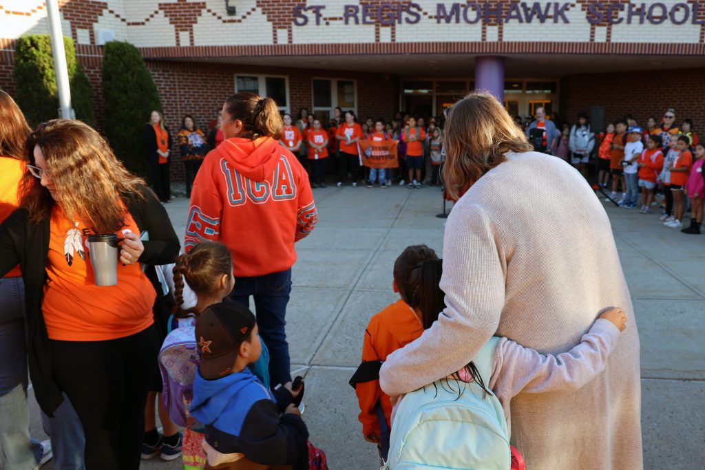 A crowd of people in a circle in front of St. Regis Mohawk School