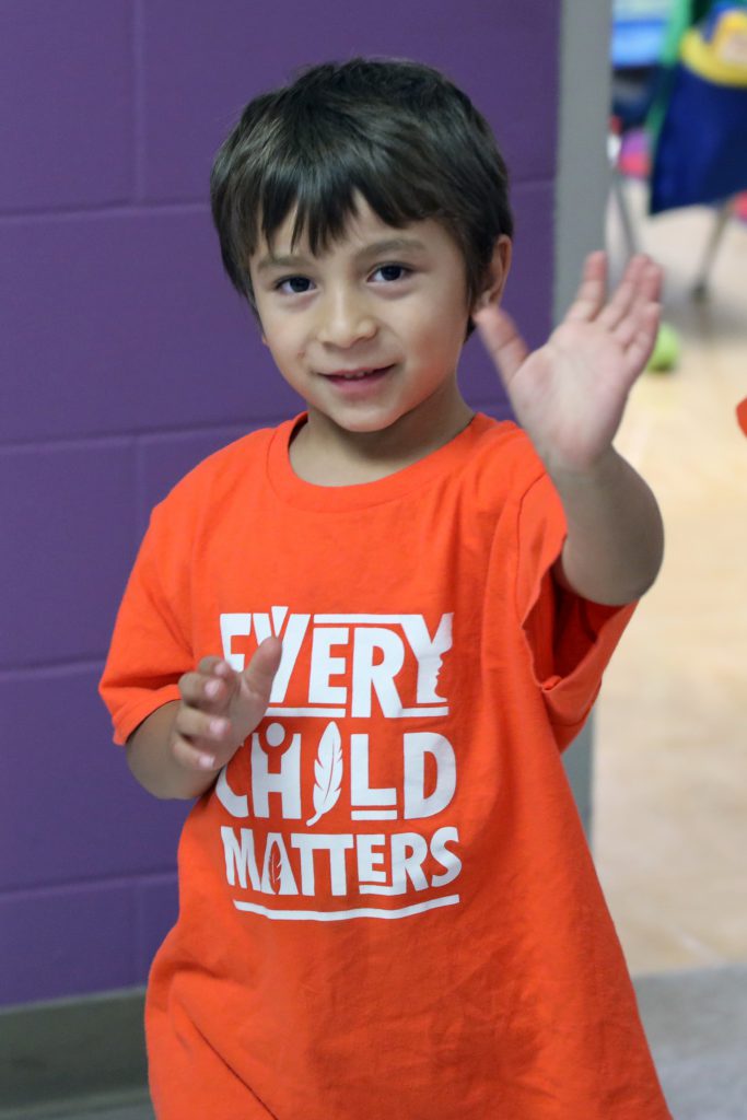 A child wearing a orange shirt that says 'Every Child Matters' waves