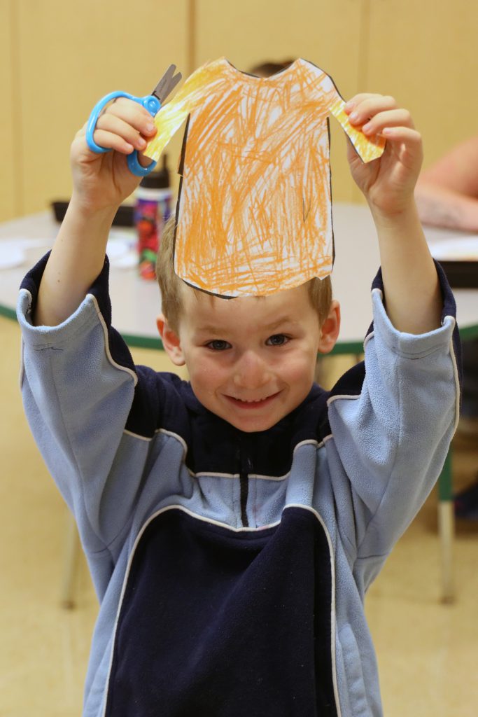 A child holds up a drawing of a orange shirt