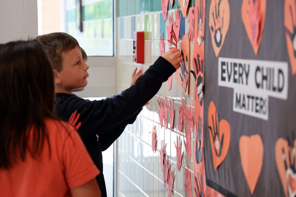 A student puts a paper cutout of a hand on a wall next to a sign that says 'Every Child Matters'