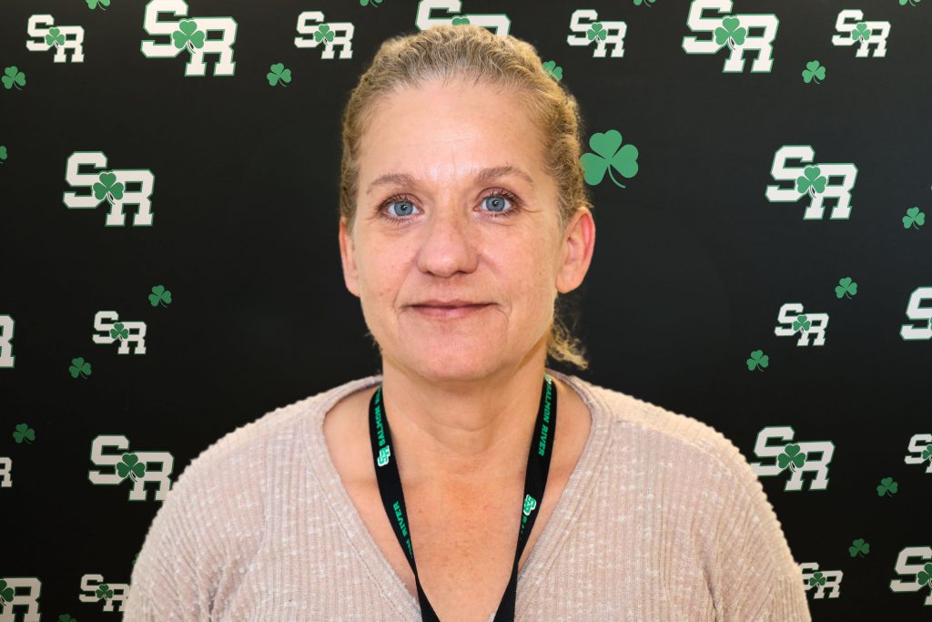 A woman smiling for a photo with a black background with green highlights with the letters 'SR'