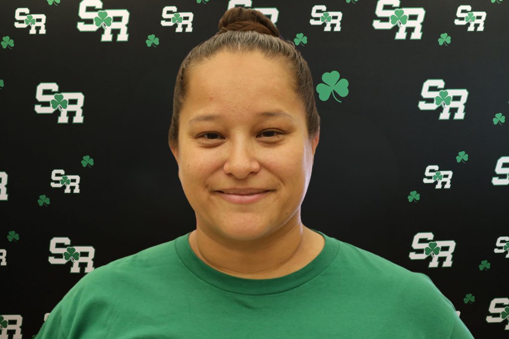 A woman smiling for a photo with a black background with green highlights with the letters 'SR'