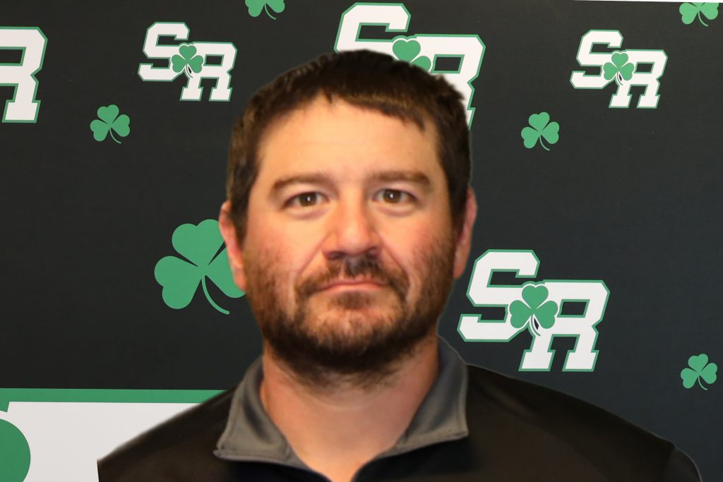 A man posing for a photo with a background that has SR written on it a few times