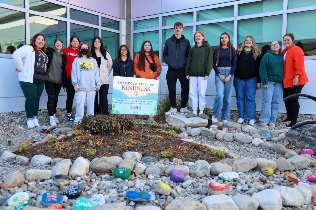 Several students standing in front of a sign that says 'Shamrock River of Kindness'