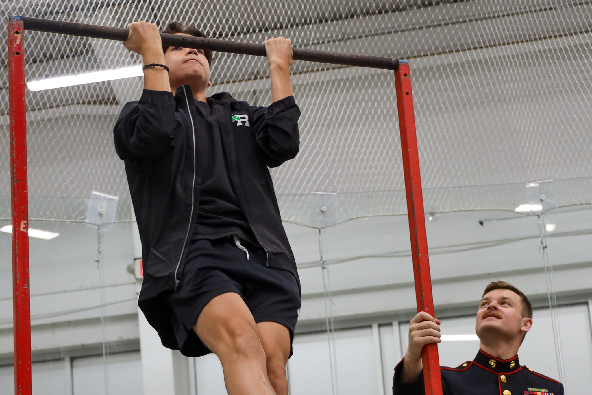 A boy lifts himself up on a bar with a member of the U.S. military looking on